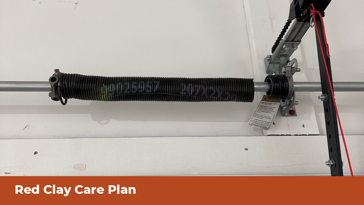 Torsion spring and opener rail inside a garage, under a Red Clay Care Plan banner
