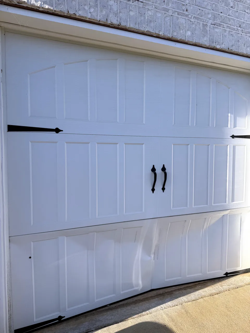 A white carriage-style garage door with dented, bowed bottom sections