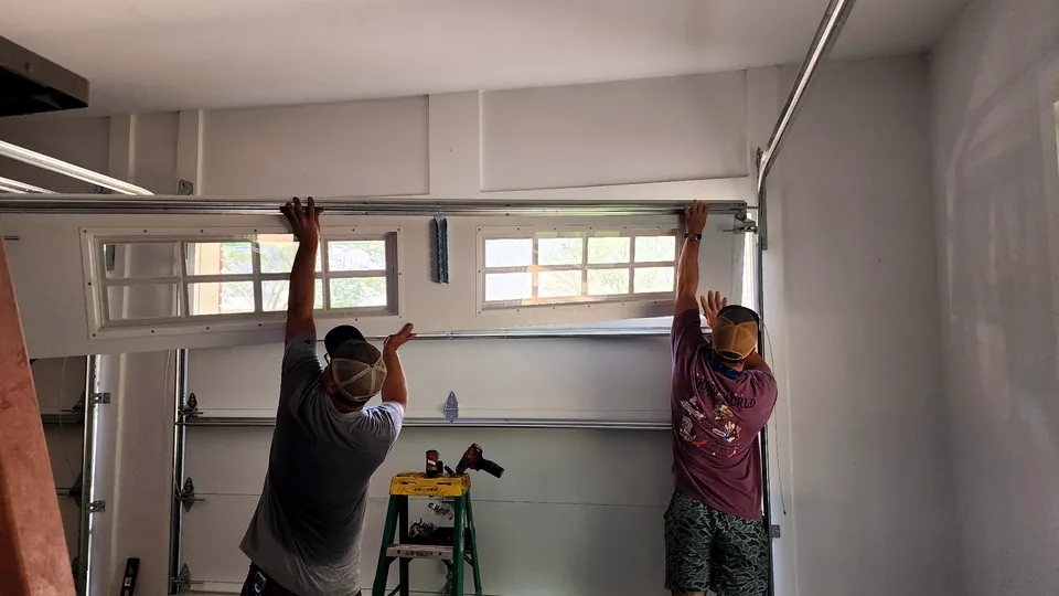 Two men lifting a garage door section into place during an install