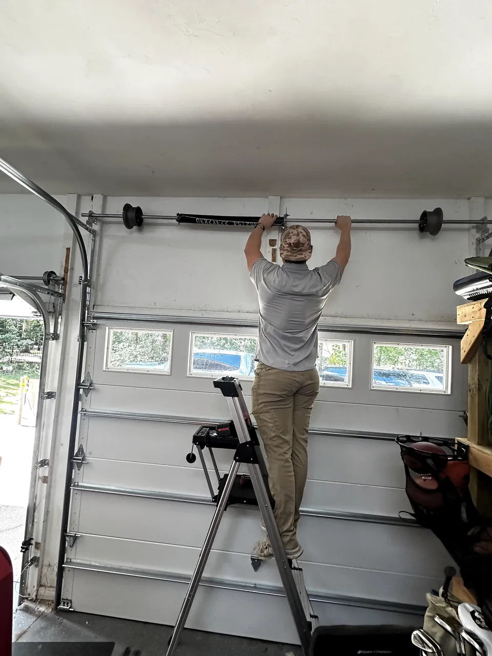 A technician on a step ladder working on high-lift track and the torsion spring above a garage door