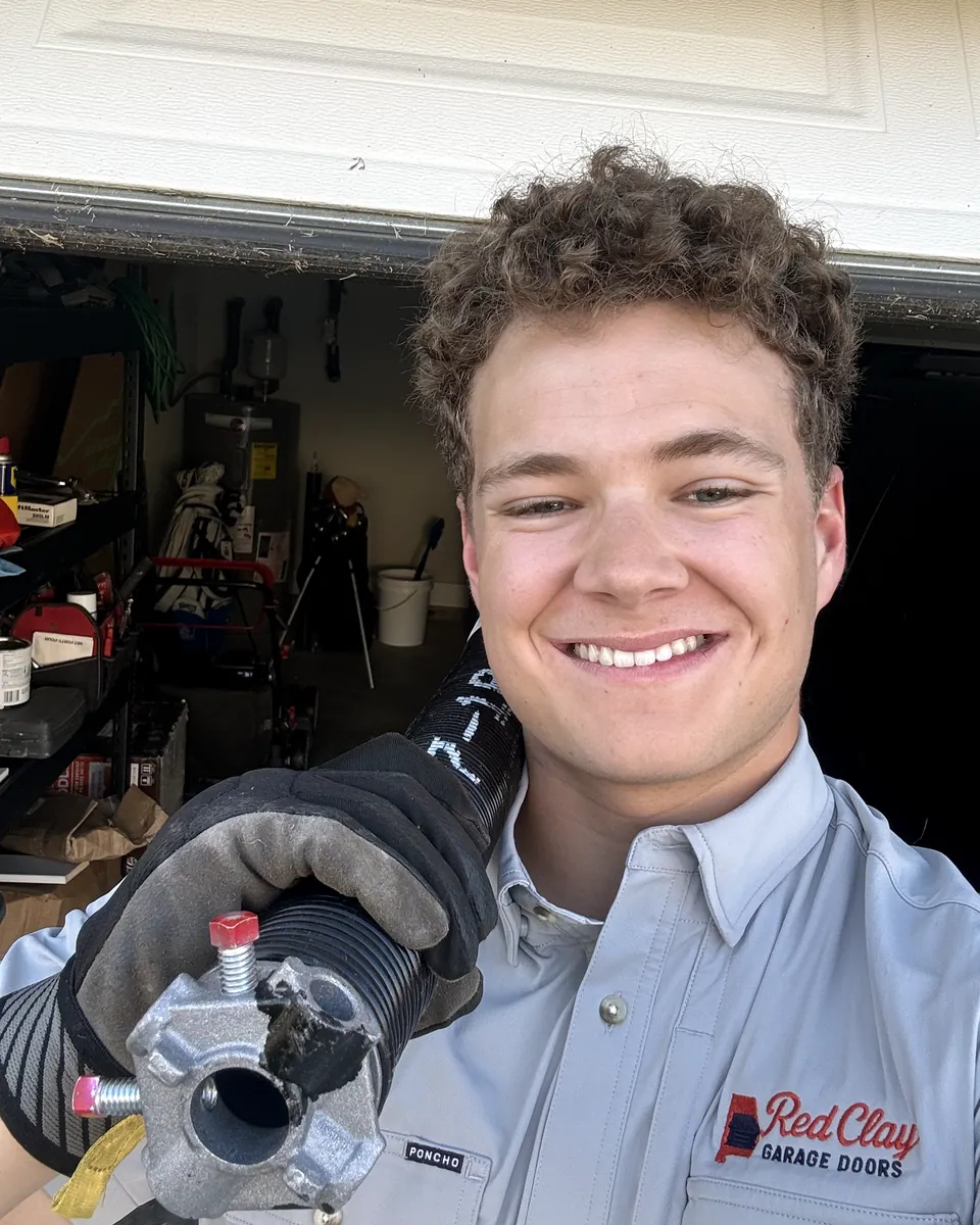 Peyton Paske, owner of Red Clay Garage Doors, smiling in a Red Clay work shirt and holding a torsion spring winding cone