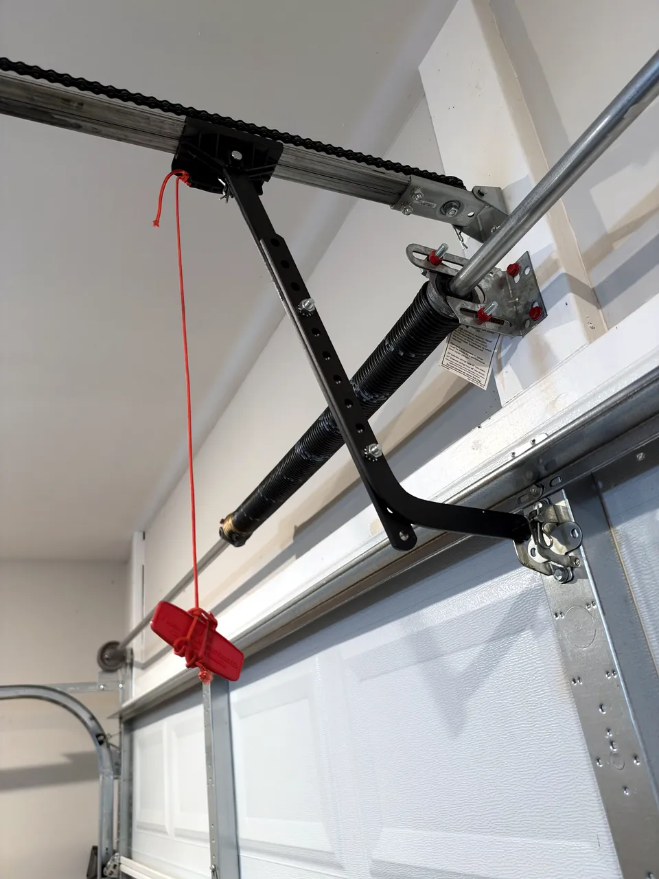 A garage door opener rail with the red emergency release handle hanging on its rope