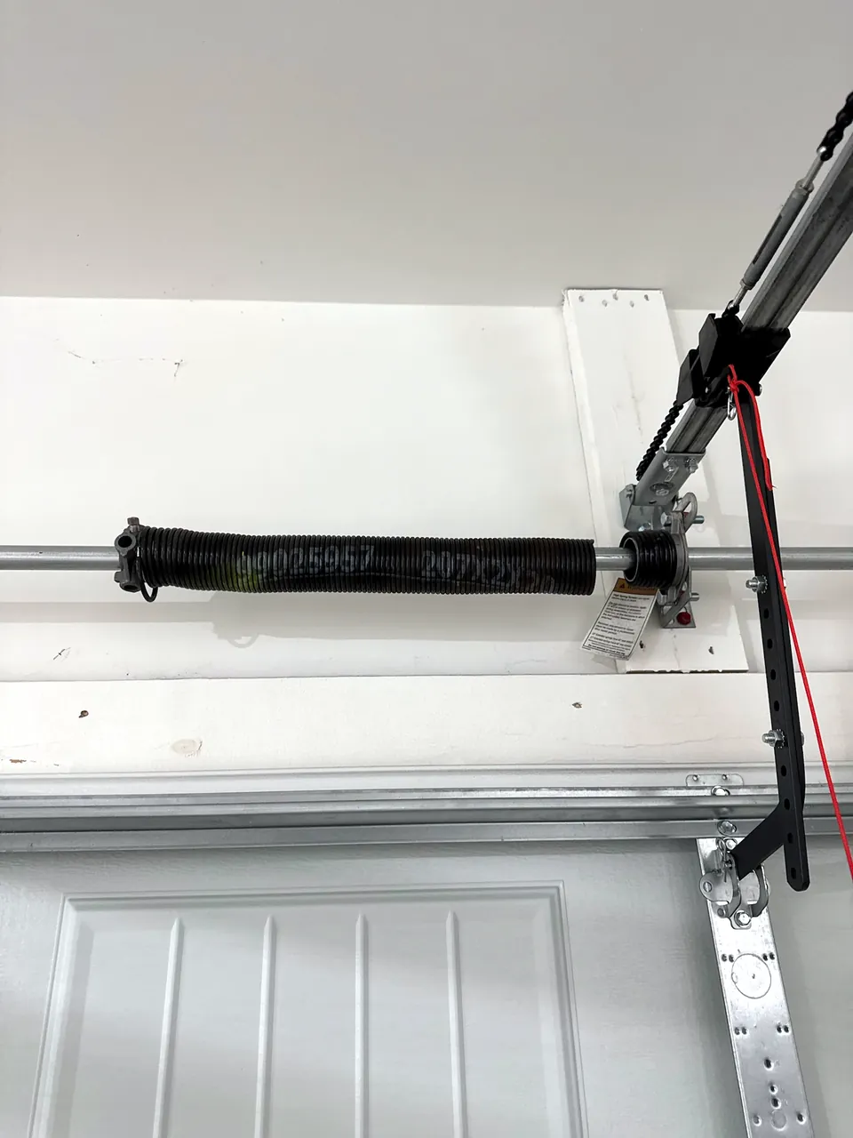 A broken torsion spring on the shaft above a white garage door, photographed by the homeowner