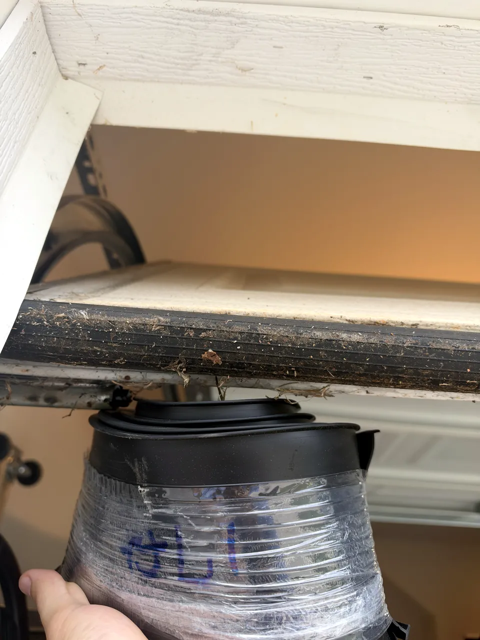 The worn, dirty bottom seal of a raised garage door, with a new roll of seal held up beside it